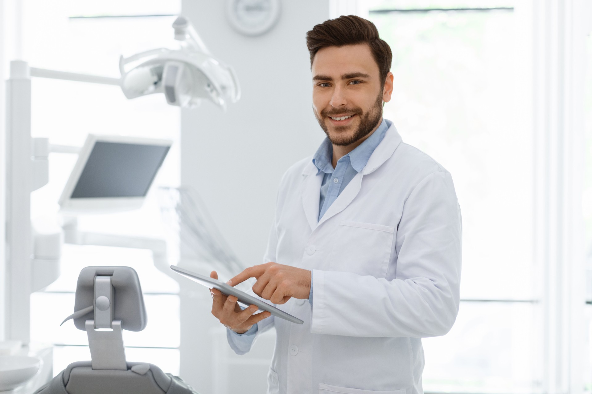 Attractive man dentist with digital tablet smiling at camera